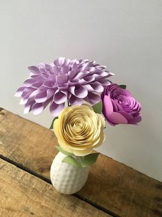 three paper flowers in a white vase on a wooden table