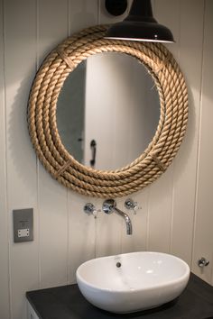 a bathroom sink under a round rope mirror