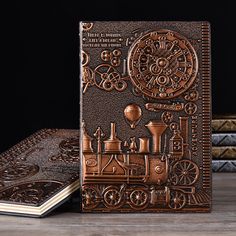 an intricately designed notebook with steam engine and gears on it, sitting next to two books