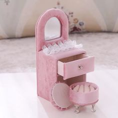 a pink jewelry box with an open drawer and mirror in it on a table next to a pillow