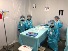 three doctors in blue scrub suits stand at a table with an iv kit on it