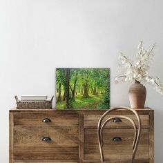 a wooden dresser with two drawers and a painting on the top, next to a vase filled with flowers