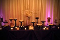 a table topped with lots of desserts and candles next to a wall covered in drapes