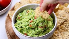 someone dipping guacamole into a bowl with tortilla chips on the side