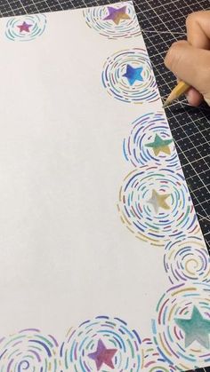 someone is writing on paper with colored circles and stars in the center, while holding a pencil