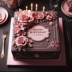 a birthday cake decorated with pink flowers and candles on top of a table next to silverware