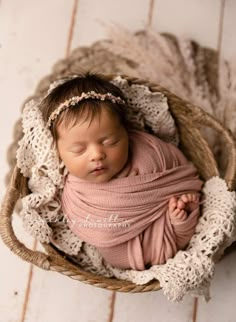 a newborn baby wrapped in a pink wrap is laying in a wicker basket on a white wooden floor