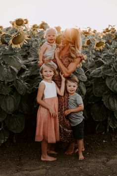 a mother and her two children standing in front of a sunflower field at sunset