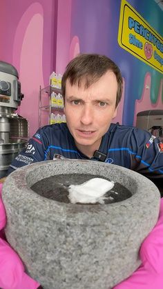 a man is holding a bowl with something in it and looking at the camera while wearing pink gloves