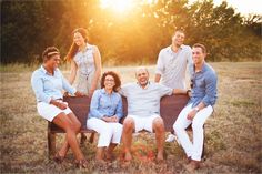 a group of people sitting on top of a wooden bench in a field at sunset