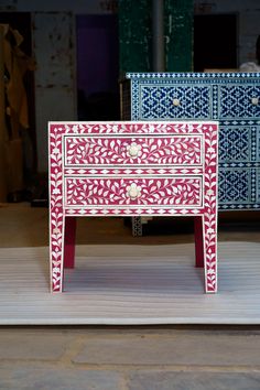 a red and white chest of drawers sitting on top of a wooden floor next to other furniture