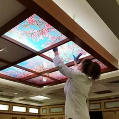 a woman in white shirt and black pants standing under a ceiling with flowers on it