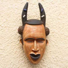 Inspired by the masks used by the Igbo people of Nigeria Ghana's Christopher Nyasafo designs a striking African mask that depicts a traditional water spirit. This hand-carved sese wood mask which features a brown rustic face has squinted eyes and black lips. The spirit's black horns are accented with four beads of recycled glass. Squinting Eyes, Black Horns, Wood Mask, Water Spirit, African Mask, Recycled Glass Bead, Black Lips, African Masks, Casual Work