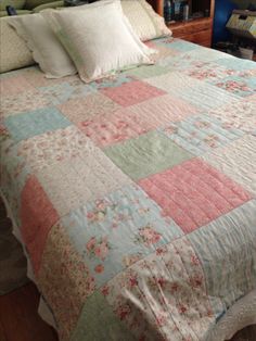 a bed with pink, blue and green bedspread on top of it in a bedroom