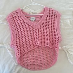 a pink crocheted sweater is hanging on a white hanger and it's made from plastic