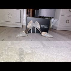 two pairs of silver high heel shoes sitting on the floor next to a shoe box