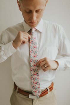 a man adjusting his tie while wearing a dress shirt and khaki pants,