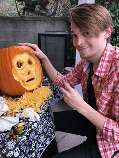 a young man carving a pumpkin with a face carved into it's head and shredded cheese on the table