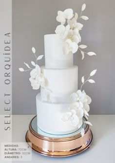 a three tiered white wedding cake with flowers on the top and bottom, sitting on a gold platter