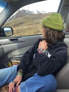 a young man sitting in the back seat of a car wearing a green beanie