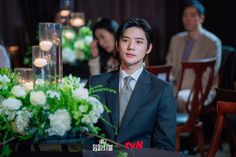 a man in a suit sitting at a table with flowers and candles on the table