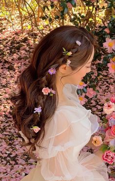 a woman with long hair and flowers in her hair sitting on the ground next to pink flowers