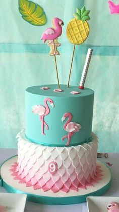 a blue cake with pink flamingos and pineapples on top is sitting on a table