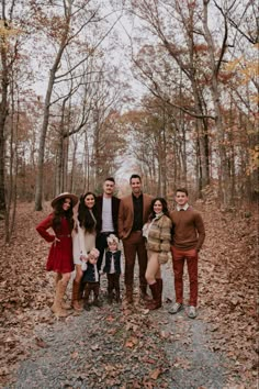 a family posing for a photo in the woods with leaves on the ground and trees around them