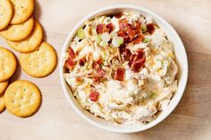 a bowl of potato salad next to crackers on a wooden table with cheese and bacon