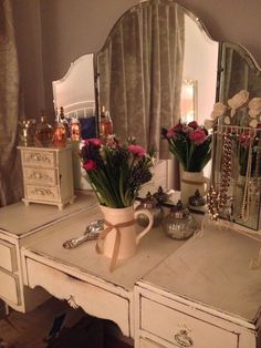 a white desk topped with a vase filled with flowers and a mirror on top of it