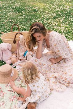 a mother and her daughter sitting on the grass with stuffed animals