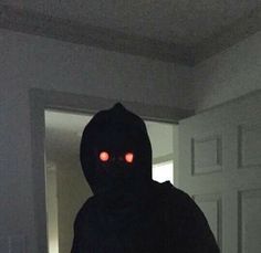 a person in a dark room with red eyes and a hoodie over their head