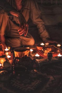 a man sitting on the floor surrounded by candles and other items in front of him