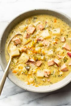 a bowl of soup with salmon and potatoes on a marble countertop next to a spoon