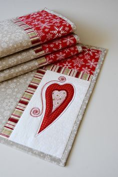 three red and white quilts are stacked on top of each other, one with a heart in the center