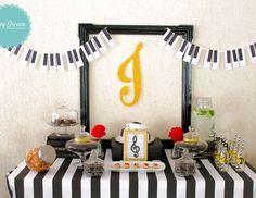 a black and white striped table cloth topped with desserts next to a piano themed wall