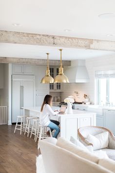 a woman sitting at a kitchen island in front of a white counter top with gold pendant lights