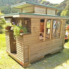 a small wooden building with plants growing out of it's windows on the grass