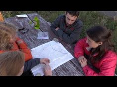 three people are sitting at a picnic table looking at a map and writing on paper