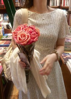 a woman holding a bouquet of flowers in her hand while standing next to a bookshelf