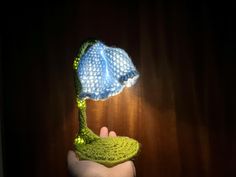 a hand holding a knitted hat on top of a wooden table next to a curtain