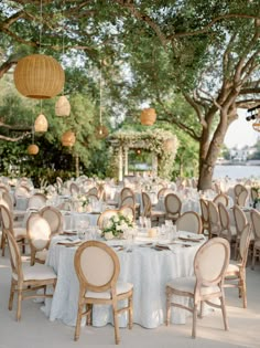 tables and chairs are set up for an outdoor wedding reception with hanging lanterns above them