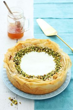 a cake on a plate next to a coffee cup and spoon with nuts in it