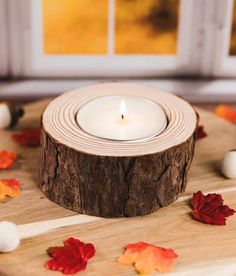 a candle that is sitting on top of a wooden table with autumn leaves around it