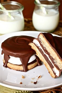 there is a chocolate sandwich on the plate with milk in the glass jars behind it