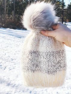 a hand holding a knitted bag with white fur on it in the snow near some trees