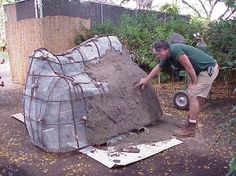 a man working on a large rock in the middle of a yard with trees and bushes behind him