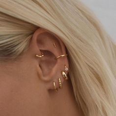 a woman with blonde hair wearing three gold ear cuffs and an earring that is shaped like a leaf