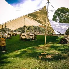 a large tent set up with tables and chairs for an outdoor function in the grass