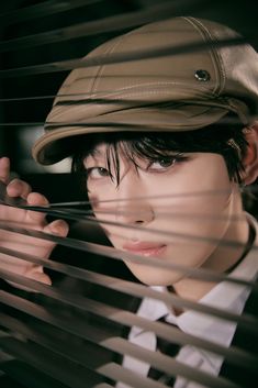 a young man wearing a hat looking through blinds